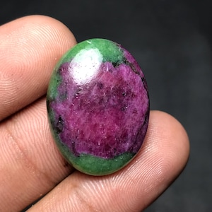 Puede incluir: Gema ovalada con una vibrante combinación de colores. El centro presenta un tono magenta intenso, rodeado por una banda verde. La superficie pulida de la piedra refleja la luz, mostrando sus patrones y texturas naturales. Una pieza única y llamativa.