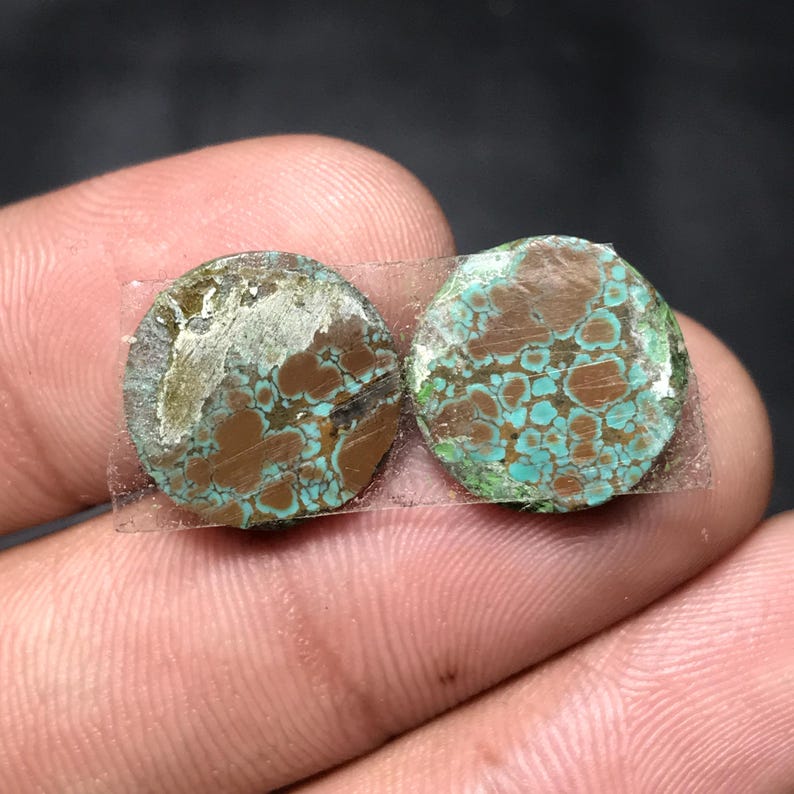 Op de afbeelding: Twee ronde, verweerde stenen in turquoise en bruin, bijeengehouden door transparante tape. De stenen hebben een gevlekt patroon met tinten blauwgroen en bruin. De randen vertonen een groenachtige tint, wat duidt op oxidatie.