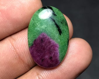 May include: Oval-shaped gemstone featuring a vibrant combination of colors. The stone showcases a rich, deep magenta hue at the base, transitioning to a bright green with black veining. The polished surface reflects light, highlighting the stone's natural beauty.