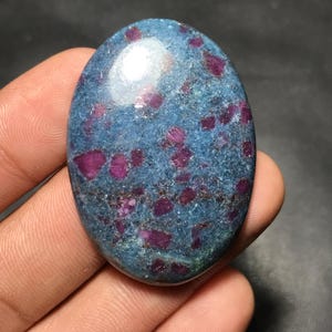 Peut inclure: Pierre précieuse ovale avec une base bleu-vert et des inclusions rouges vives. La surface polie reflète la lumière, soulignant les motifs et couleurs naturels de la pierre. Une pièce unique et attrayante pour bijoux ou collection.