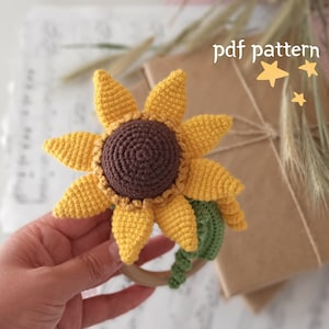 May include: Crochet sunflower rattle toy with a wooden ring and green leaves. The sunflower is yellow with a brown center. The toy is handmade and perfect for babies.