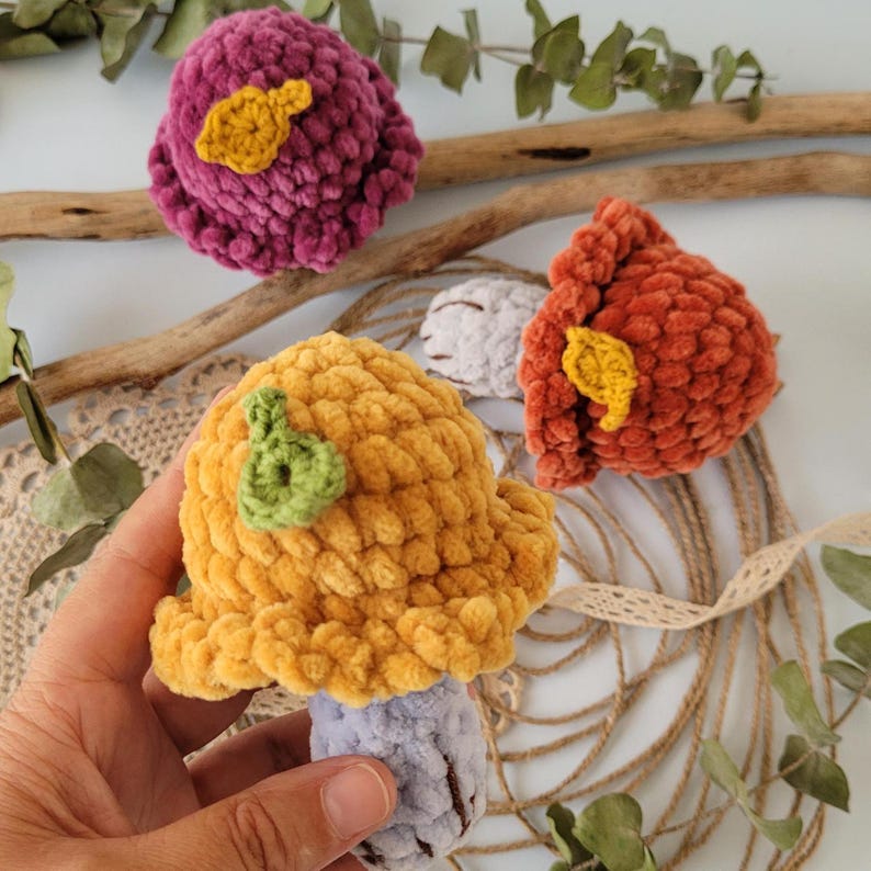 May include: Three crocheted mushroom toys. One is yellow with a green leaf, one is red with a yellow leaf, and one is purple with a yellow leaf.