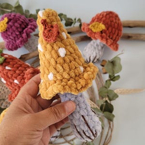 May include: A set of four crocheted mushrooms in various colours, including orange, purple, and yellow. The mushrooms have white polka dots and are made with a fuzzy yarn.