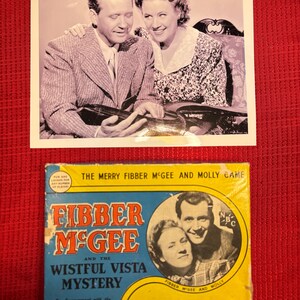 May include: A black and white photograph of a smiling couple, and a vintage game box. The game box is titled "Fibber McGee and the Wistful Vista Mystery" with the NBC logo. The box is yellow and blue.