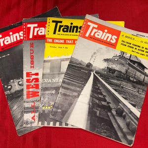 May include: A collection of vintage "Trains" magazines, featuring vibrant red, yellow, and black covers. The magazines showcase images of trains and railway scenes, with text including "The Magazine of Railroading" and issue dates.