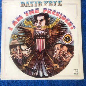 May include: A vintage vinyl record album cover featuring a cartoon illustration of a bald eagle with the words "I AM THE PRESIDENT" surrounding it. The eagle is holding a flag with stars and stripes. The album cover is titled "David Frye".