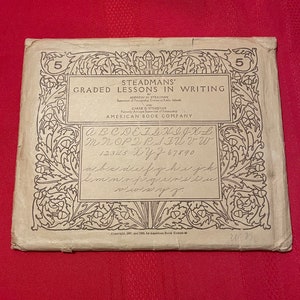 Puede incluir: Una cubierta de libro vintage para "Steadmans' Graded Lessons in Writing" de Andrew H. Steadman y Carrie D. Steadman. La cubierta presenta un borde decorativo con un diseño floral y el texto "American Book Company".
