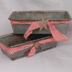 May include: Two rustic metal loaf pans with red and white gingham ribbon and metal star accents.