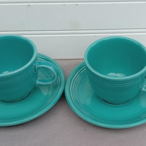 May include: Two turquoise teacups and saucers. The cups have a rounded shape and a simple design. The saucers have a scalloped edge.