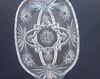 May include: A clear glass divided serving dish with a starburst pattern. The dish has two sections and two handles.