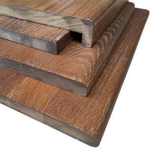 Puede incluir: Primer plano de tres tablas de madera con un acabado marrón intenso. Las tablas tienen un patrón de vetas de madera natural y bordes redondeados. La tabla superior tiene un diseño escalonado único. La madera parece estar teñida o tratada.