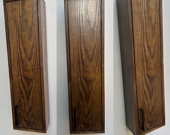 May include: Three dark brown wooden wall cabinets with black metal handles. The cabinets are mounted on a white wall.