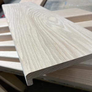 May include: A close-up of a light wood stair tread with a rounded edge. The wood grain is visible and the tread has a light, natural finish.