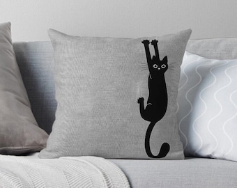 May include: A black cat silhouette hanging upside down from a surface, with its tail curled around its body. The cat has a simple, cartoon-like design with large eyes and a small mouth.