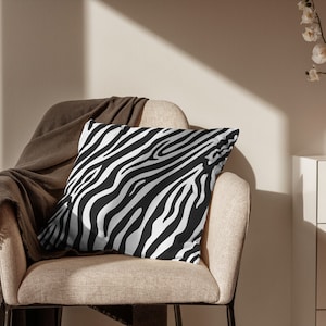 Puede incluir: Un cojín decorativo con estampado de cebra en blanco y negro sobre un sillón beige con una manta de lana marrón.