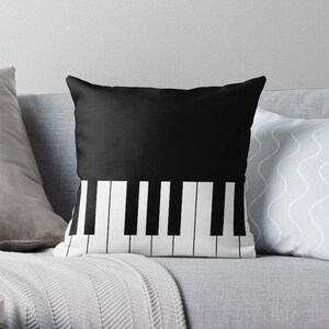 Puede incluir: Almohada de color negro y blanco con un diseño de teclado de piano. La almohada es negra con teclas blancas en la parte inferior.