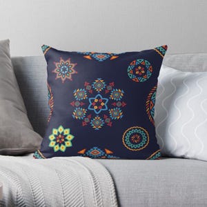 Puede incluir: Una almohada con un fondo azul marino y un patrón geométrico colorido. El patrón presenta círculos, estrellas y diamantes en tonos de azul, verde, amarillo, naranja y rojo.