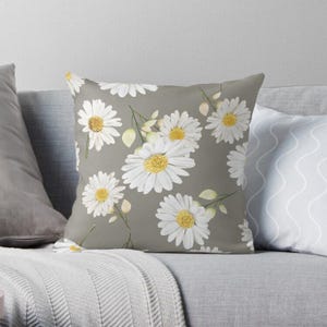 Puede incluir: Una almohada con un fondo gris y un patrón de margaritas blancas. Las margaritas tienen centros amarillos y están dispuestas en un patrón repetitivo.