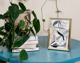 May include: A teal blue metal side table with a framed abstract art print and a potted plant. The plant has long green leaves and vines climbing the wall. A stack of books is on the table.