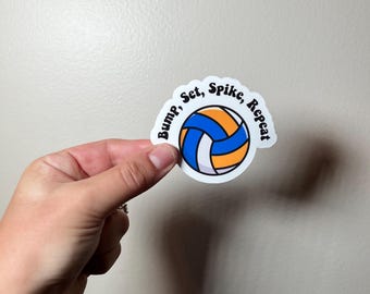 May include: A white sticker with a volleyball design. The volleyball is blue, orange, and white. The sticker has the words "Bump, Set, Spike, Repeat" in black, curved around the volleyball.