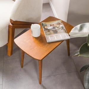 May include: A wooden side table with a curved top and four legs. A magazine and a white mug are on the table.