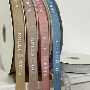 May include: Five spools of ribbon in different colors: beige, brown, pink, blue, and gray. Each spool has the text "BELLE & B&Ecirc;TE" printed on it.