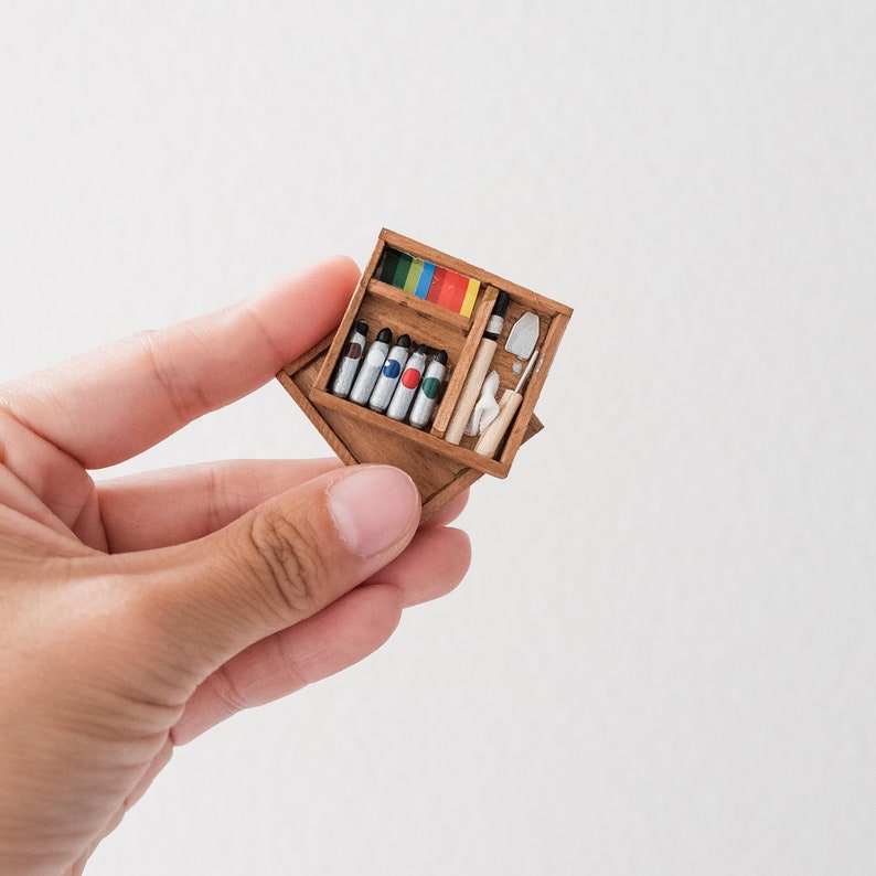 May include: A wooden box with a hinged lid, containing a set of paint tubes, a small trowel, and a paintbrush. The box is open and the contents are visible.