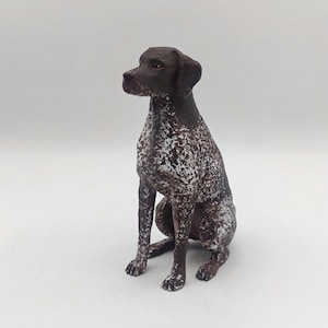 Op de afbeelding: Een bruin en wit Duitse Korthaar-beeldje dat zit met zijn hoofd naar links gedraaid. Het beeldje is gemaakt van een bruin en wit gevlekt materiaal.