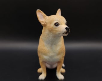 May include: A small, tan-colored Chihuahua figurine with a white chest and paws. The dog is sitting upright with its ears perked up and eyes looking to the side. The figurine has a glossy finish and is set against a dark background.