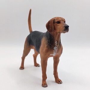 Op de afbeelding: Een bruine en zwarte speelgoedhond met witte markeringen. De hond staat met zijn kop naar rechts gedraaid en zijn staart omhoog.