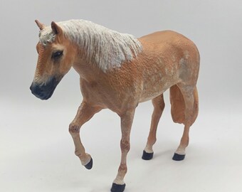 May include: A light brown toy horse with a white mane and tail. The horse has black hooves and is standing on a white background.