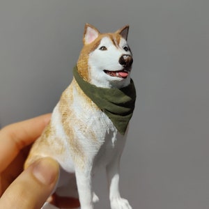 May include: A 3D printed figurine of a husky dog wearing a green bandana. The dog is sitting with its head tilted up and its tongue sticking out.