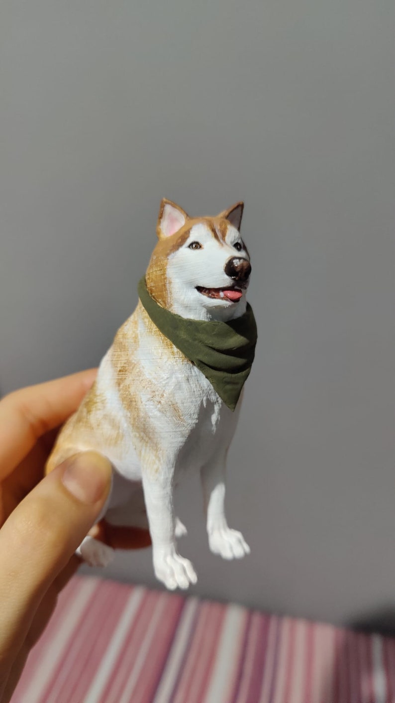 May include: A 3D printed figurine of a husky dog wearing a green bandana. The dog is sitting with its head tilted up and its tongue sticking out.