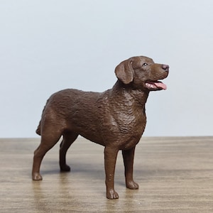 May include: A brown, furry dog figurine standing on a wooden surface. The dog is looking to the right with its mouth open.