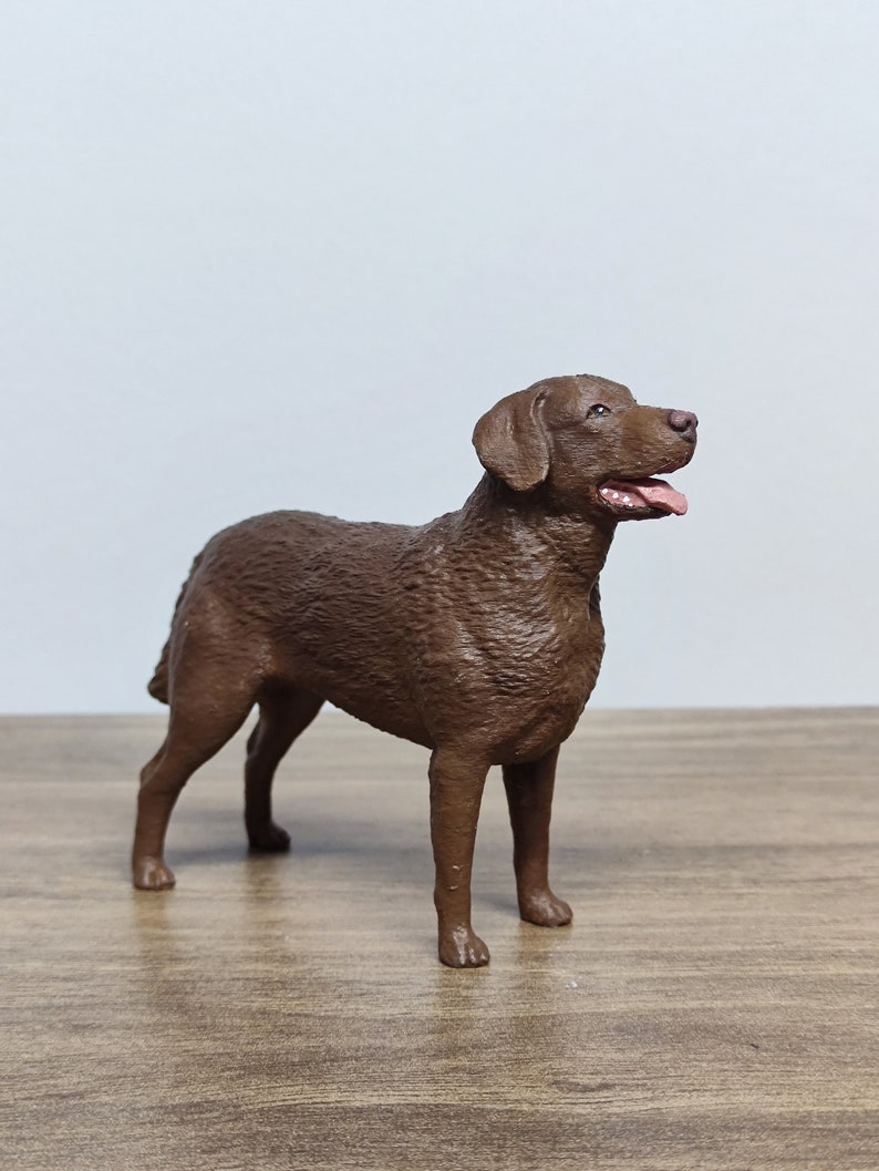 May include: A brown, furry dog figurine standing on a wooden surface. The dog is looking to the right with its mouth open.