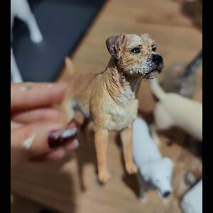 Könnte beinhalten: Eine handbemalte Figur eines braunen und weißen Hundes mit kurzem, drahtigem Fell. Der Hund steht auf allen vieren und hat den Kopf zur Seite geneigt. Die Figur ist sehr detailliert und realistisch.