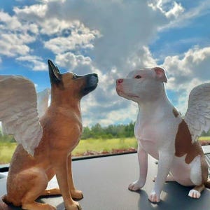 Könnte beinhalten: Zwei 3D-gedruckte Hundefiguren mit Flügeln. Die Hunde sitzen und schauen sich an. Der Hund links ist braun und der Hund rechts ist weiß mit braunen Flecken.