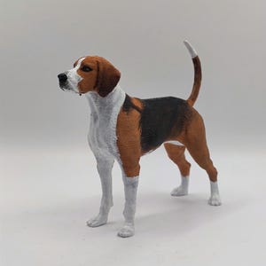 May include: A brown, black, and white painted figurine of a Bloodhound dog standing on a white surface.