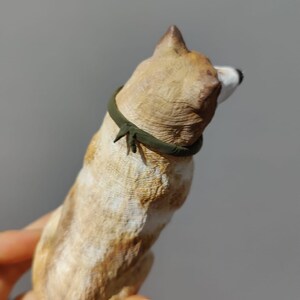 May include: A small, tan and white ceramic dog figurine with a green collar. The figurine is standing on its hind legs and is looking to the side.