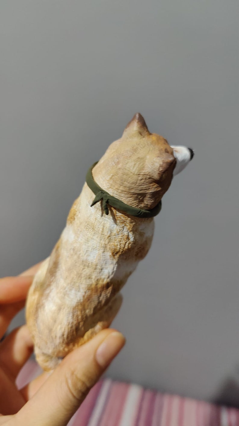 May include: A small, tan and white ceramic dog figurine with a green collar. The figurine is standing on its hind legs and is looking to the side.