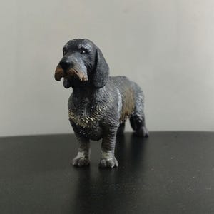 May include: A miniature Dachshund dog figurine. The dog is predominantly black with a brown and grey textured coat. It is posed standing on all fours, with its head turned slightly to the side. The figurine has a realistic appearance.