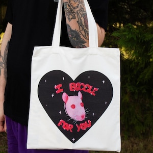 Pode incluir: Sacola branca de tecido com um design de coração preto. O coração contém um rato rosa e o texto "I Boggle For You" em letras vermelhas.