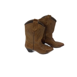 May include: A pair of brown leather cowboy boots. The boots feature a pointed toe, decorative stitching, and a short heel. The boot shafts are mid-calf length. The boots are set against a white background.