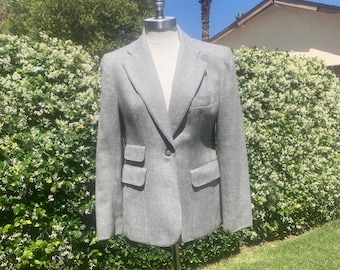 Puede incluir: Un blazer gris y blanco con estampado de pata de gallo exhibido en un maniquí. El blazer tiene solapas con muescas, cierre de un solo botón y dos bolsillos delanteros. La chaqueta está confeccionada con un corte clásico.