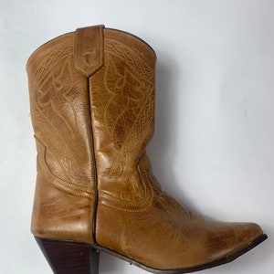 May include: A single tan leather cowboy boot with decorative stitching. The boot has a pointed toe and a dark brown heel. The leather appears worn, giving it a vintage look. The boot is set against a white background.