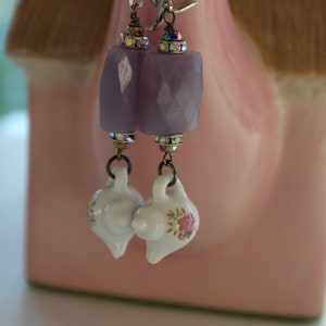May include: Purple and white porcelain teapot earrings with a floral design. The earrings are made with a purple faceted stone and a silver hook.
