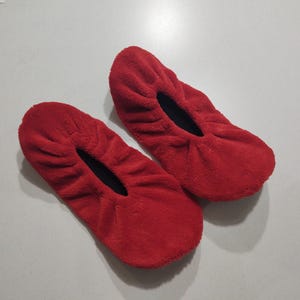 May include: A pair of red fleece slipper socks. The socks are made of a soft, fuzzy material and have a black elastic band around the opening.