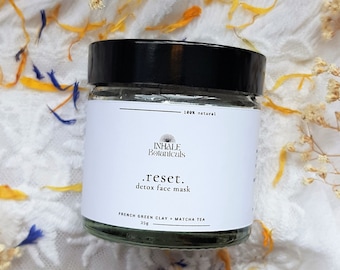 May include: A white jar with a black lid and a green label. The label reads "INHALE Botanicals .reset. detox face mask FRENCH GREEN CLAY + MATCHA TEA 35g 100% natural".