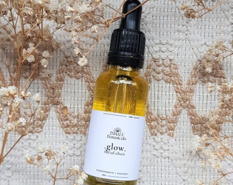 May include: A glass bottle of facial elixir with a black dropper top. The bottle is labeled "INHALE Botanicals .glow. facial elixir POMEGRANATE + AVOCADO 30ml".