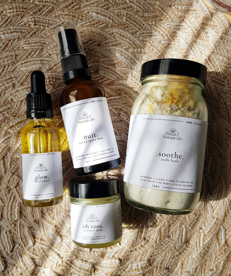 May include: Four glass bottles with labels containing natural beauty products. The products are labeled "glow. facial elixir", "nuit. sacred space mist", "oh rosa. treatment balm", and "soothe. milk bath".
